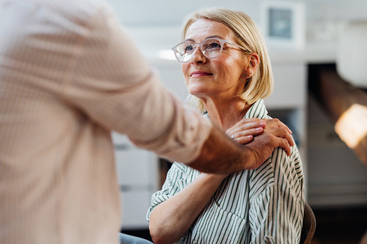 A middle aged woman sitting and looking at someone who's putting their hand on her shoulder after she got BHRT in Sequim.